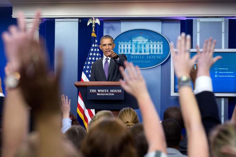 Barack Obama at a podium with hands raised in foreground.
